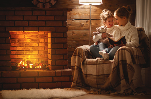 happy family mother and child daughter read a book on winter autumn evening near fireplace