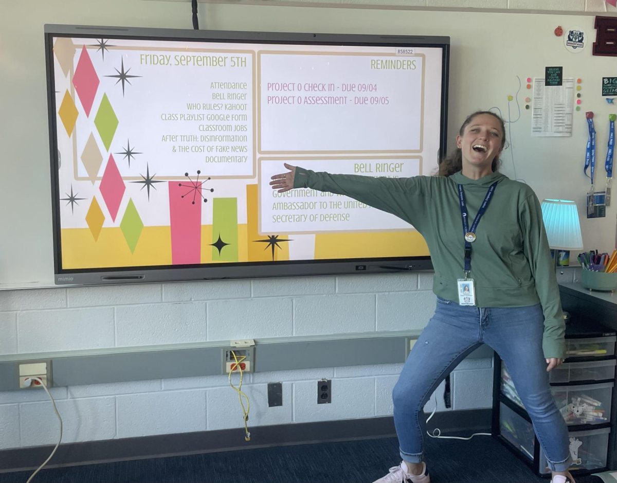 Ms. Rausch standing excitedly in front of the board in her classroom! 